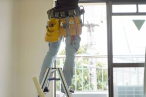 脚立に乗り工具で室内作業をする男性